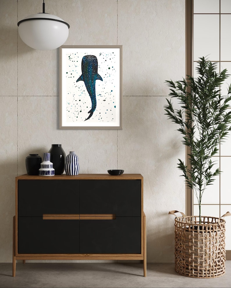 May include: Framed art print featuring a whale shark illustration. The artwork depicts the whale shark in shades of blue with a speckled pattern, set against a white background with scattered green and blue paint splatters. The frame is a neutral color.