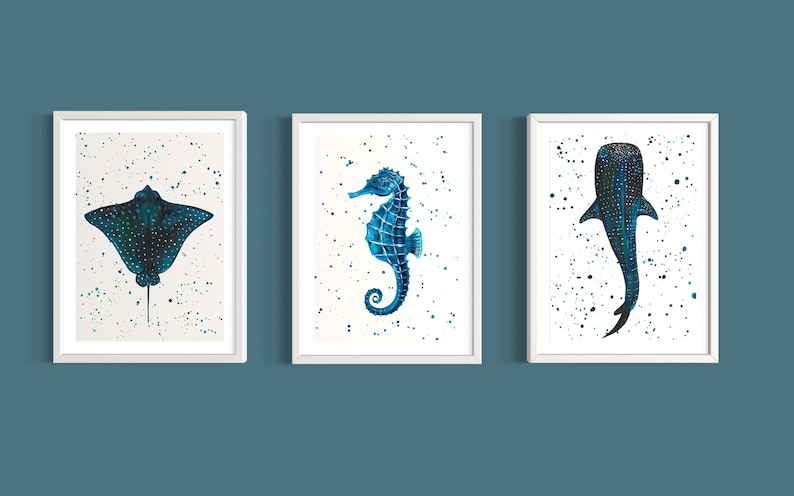 May include: Three framed art prints featuring watercolor illustrations of marine life. The set includes a stingray, a seahorse, and a whale shark, each in shades of blue and teal against a white background with speckled accents.