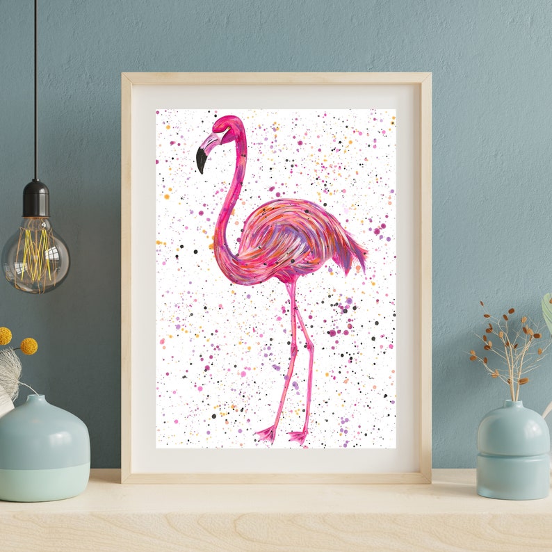 May include: A pink flamingo with a white background and colorful splatter paint. The flamingo is standing on one leg and has its head turned to the side.