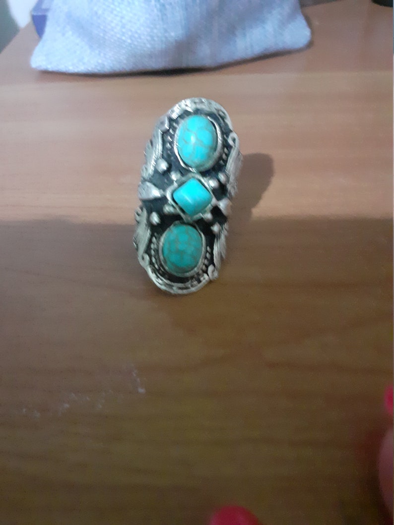 Op de afbeelding: Een zilveren ring met drie turquoise stenen in een decoratief ontwerp.