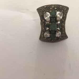 Può includere: Un anello d'argento con un design geometrico con pietre verdi e bianche.