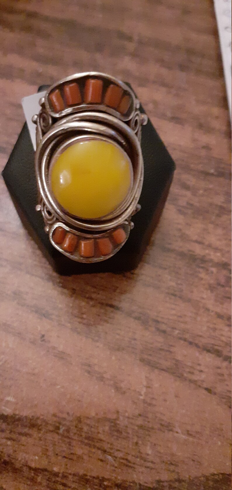 Puede incluir: Un anillo de plata con una piedra amarilla grande engastada en el centro. El anillo est&aacute; decorado con una banda de peque&ntilde;as piedras naranjas.