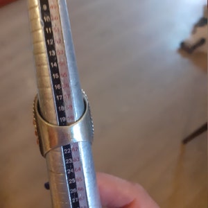 May include: A silver ring sizer with red and white stones. The sizer is marked with numbers from 6 to 31.