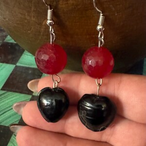 May include: A pair of dangle earrings with red and black beads. The red beads are faceted and the black beads are heart-shaped.