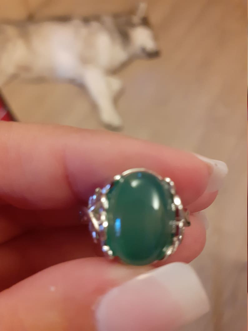 May include: A silver ring featuring a green oval gemstone set in a delicate filigree design.