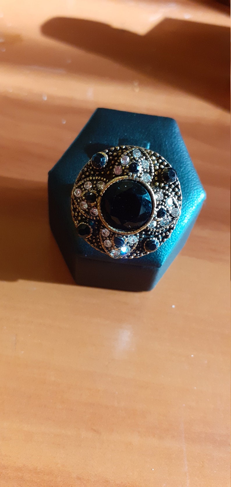 May include: A gold ring with a large black gemstone surrounded by smaller black and white gemstones. The ring is displayed on a dark blue velvet ring box.