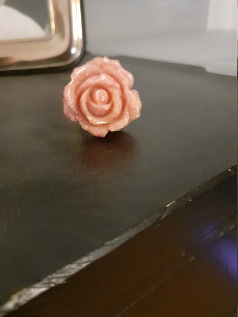 Op de afbeelding: Een roze roos gesneden uit steen. De roos heeft een gedetailleerd ontwerp en een glanzende afwerking.