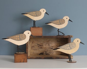 Puede incluir: Cuatro esculturas de pájaros de madera con patrones decorativos en las alas y picos y patas negros. Las aves se exhiben sobre bloques de madera y una caja de madera rústica sobre un fondo azul. Las aves miden aproximadamente 15 cm de largo.