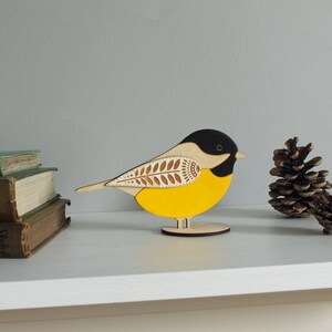 May include: A yellow and black wooden bird figurine with a white and brown patterned wing. The bird is standing on a wooden base.