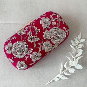 May include: A vibrant pink velvet clutch with silver floral embroidery and sequins. The clutch has a gold clasp.
