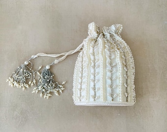 May include: A white beaded drawstring bag with two white tassel pulls. The bag is decorated with a pattern of white beads and silver accents.