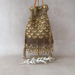 Könnte beinhalten: Eine goldene Clutch-Tasche mit Perlenbesatz und Fransen. Die Tasche ist mit einem Muster aus überlappenden Schuppen verziert.