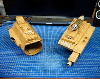 May include: Two cardboard models of spaceships, one with a pointed nose and the other with a rounded nose, are displayed on a blue cutting mat.