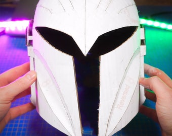 May include: A white cardboard helmet with a black visor and a detailed design. The helmet is being held by hands and is partially open.