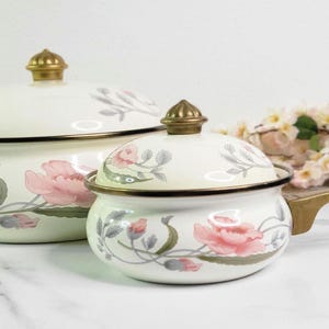 May include: Two white enamel pots with floral designs and gold accents. The larger pot has a lid and the smaller pot has a handle.