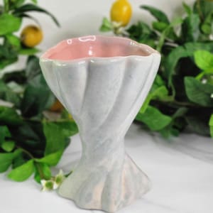 May include: A ceramic vase with a light blue and pink color scheme. The vase has a twisted, fluted design and a flared base. The interior is a soft pink. The vase is a decorative item, suitable for displaying flowers or as a standalone accent piece.