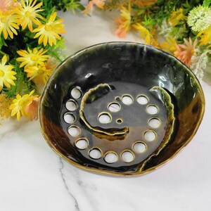May include: A dark green and brown ceramic soap dish with a swirl design and multiple drainage holes.