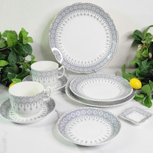 May include: A white porcelain tea set with a gray and white decorative border. The set includes teacups, saucers, plates, and a serving dish. The plates are round, and the teacups have handles. The set is arranged on a white surface.