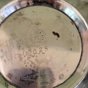 May include: Close-up of the bottom of a silver-plated pitcher with the inscription "Triple Plate Silver Plate Co.  Wilcox,  Riden, Conn." and the number "5025".