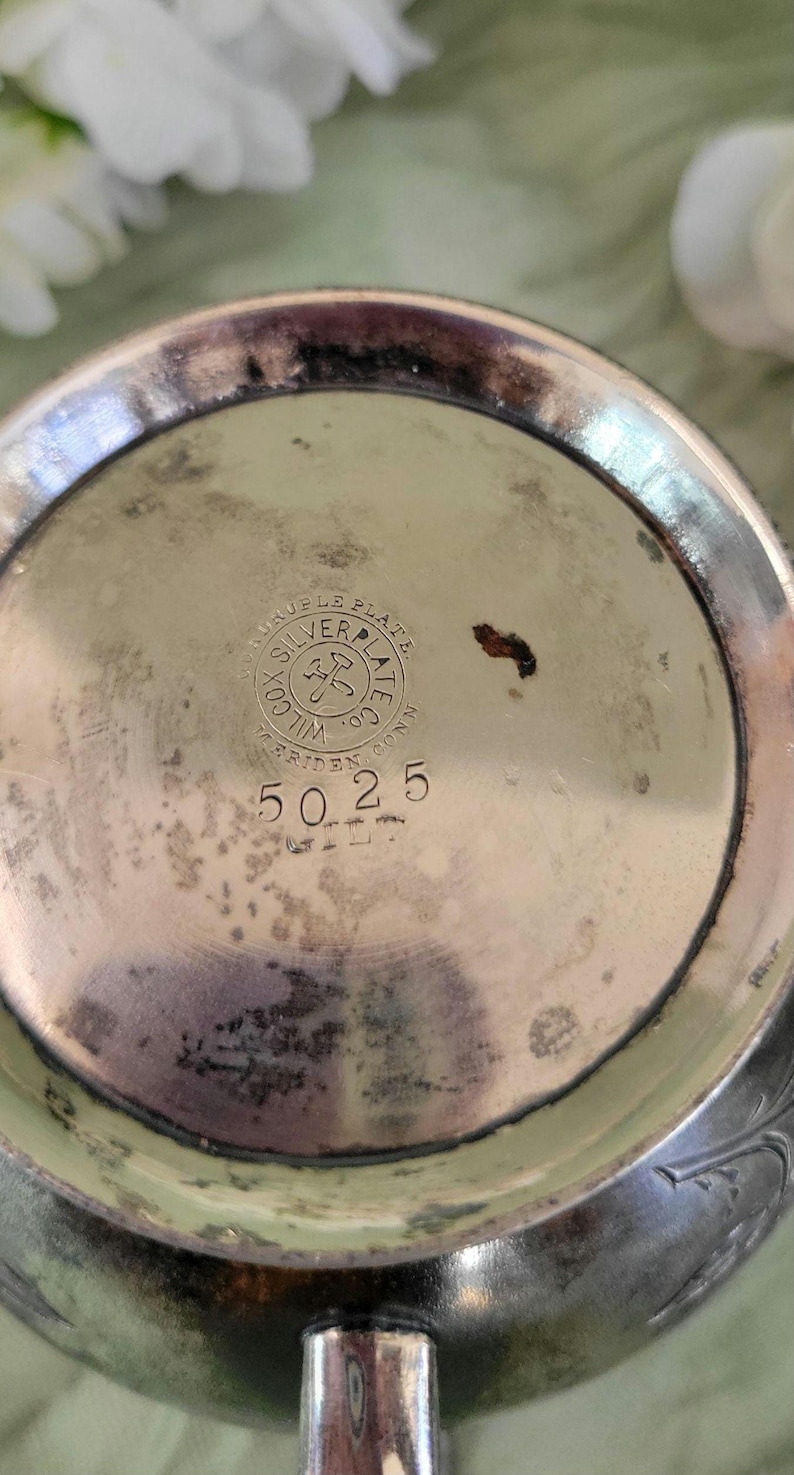 May include: Close-up of the bottom of a silver-plated pitcher with the inscription "Triple Plate Silver Plate Co.  Wilcox,  Riden, Conn." and the number "5025".