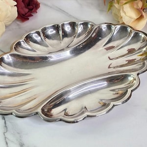 May include: A silver-colored, divided serving dish with a scalloped edge. The dish has three sections and a reflective surface. Decorative flowers are in the background.