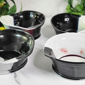 May include: Four ceramic bowls with a unique design. Each bowl features a black and white color scheme, with a glossy finish. The bowls have a curved shape and are suitable for serving various dishes. The bowls are arranged on a white surface.
