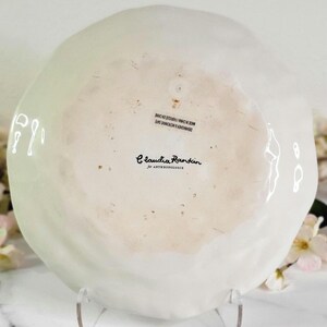 May include: White ceramic plate with a slightly rippled surface. The plate has a black inscription that reads "Claudia Rankin for Anthropologie" and "DISHWASHER & MICROWAVE SAFE MADE IN CHINA/FABRIQUE EN CHINE".