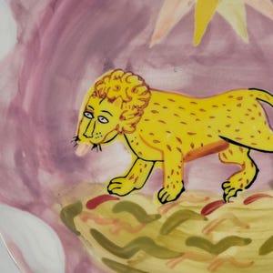 May include: A pink ceramic plate with a yellow lion and a yellow sun with a face painted on it.