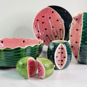 May include: A set of watermelon-themed ceramic kitchenware, including a large bowl, a pitcher, a small bowl, and two salt and pepper shakers. The pieces are all decorated with a realistic watermelon design, featuring green rind, red flesh, and black seeds.