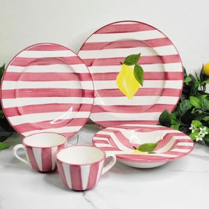 May include: A set of ceramic tableware featuring a red and white striped pattern. The set includes plates, bowls, and cups. One plate has a yellow lemon illustration. The tableware is designed for dining and serving.