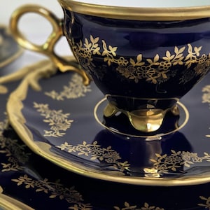 May include: A navy blue teacup and saucer set with gold floral detailing. The cup has a gold handle and trim, and the saucer has a matching gold rim. The set is elegant and classic, perfect for a tea party.