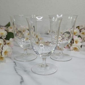 May include: A set of three ceramic mugs with a speckled, cream-colored glaze. Each mug features a different hand-painted floral design in shades of blue, green, and yellow. The mugs are approximately 4 inches tall.