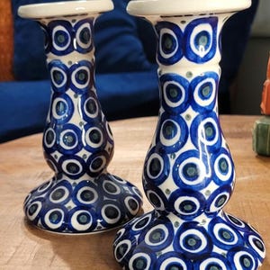 May include: A pair of blue and white ceramic candle holders with a circular pattern. The candle holders are tall and slender with a wide base.