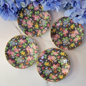 May include: Four floral patterned teacups with gold trim. The cups have a black background with pink, yellow, and blue flowers.