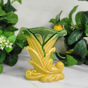May include: A vintage ceramic vase in a stylized floral design. The vase features a yellow body with green accents on the rim and interior. The vase has a flared top and a curved base, with a glossy finish.