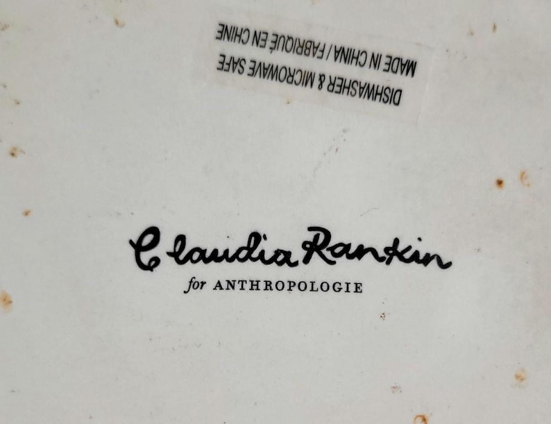 May include: A white ceramic dish with black text that reads "Claudia Rankin for Anthropologie". The dish is microwave and dishwasher safe and made in China.