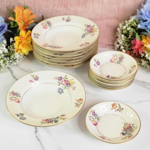 May include: A set of vintage floral patterned soup bowls and plates. The bowls and plates are white with a gold trim and feature a colorful floral design. The set includes 12 soup bowls and 12 plates.
