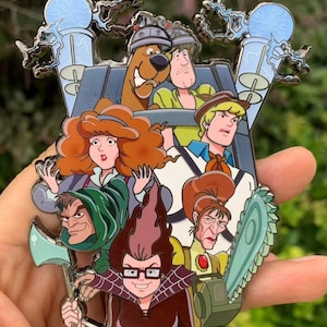Könnte beinhalten: Ein farbenfroher Emaille-Pin mit Figuren aus der Zeichentrickserie Scooby-Doo. Der Pin zeigt Scooby-Doo, Shaggy, Fred, Daphne, Velma und Bösewichte mit einer Axt und einer Kettensäge. Der Pin hat einen silbernen Metallrand und wird in einer Hand gehalten.