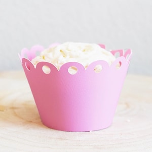 May include: Pink cupcake liner with a scalloped edge and white frosting. The liner is made of paper and has a delicate, feminine design.