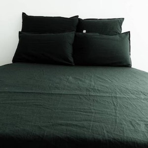 Puede incluir: Una cama verde oscuro con un edredón verde oscuro y cuatro almohadas verde oscuro. La cama está hecha con ropa de cama lisa y sin arrugas.