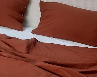 May include: A rust-colored bed with a white fitted sheet and two rust-colored pillowcases. The bed is made with a rust-colored duvet cover.