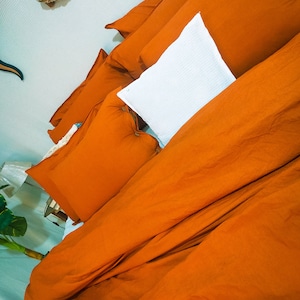 Op de afbeelding: Een bed met oranje beddengoed en een wit kussen. Het beddengoed is gemaakt van een zachte, comfortabele stof en heeft een ontspannen, casual uitstraling.