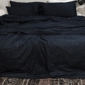 May include: A dark blue duvet cover and pillowcases are neatly arranged on a bed. The bedding is smooth and wrinkle-free, creating a clean and minimalist aesthetic.