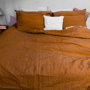 May include: A brown linen duvet cover with a white pillow and a few patterned pillows on a bed.