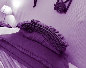 May include: A set of purple bedding including a fitted sheet with elasticized edges and two matching pillowcases. The fabric has a visible woven texture. A small dark plaque on the wall displays the text ANTARMANA JAIPUR MARK.