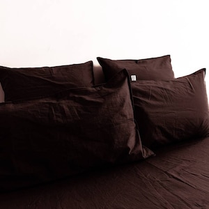 May include: A bed with a dark brown duvet cover and four dark brown pillows. The pillows are arranged in a stack of two, with the top two pillows slightly overlapping the bottom two pillows.