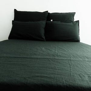 Op de afbeelding: Een donkergroen bed met een zwarte linnen dekbedovertrek en vier zwarte kussens. Het bed is opgemaakt met fris, kreukvrij linnen.