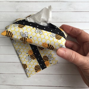 May include: A yellow and black tissue box cover with a honeycomb pattern and bees. The cover has a black ribbon with white polka dots.