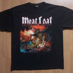 Può includere: Maglietta nera con una stampa grafica di una scena fantasy con una creatura alata, una donna con una spada e il testo "Meat Loaf".