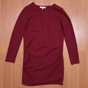 May include: A long-sleeved burgundy dress with a round neckline. The dress has a slightly gathered look in the front.